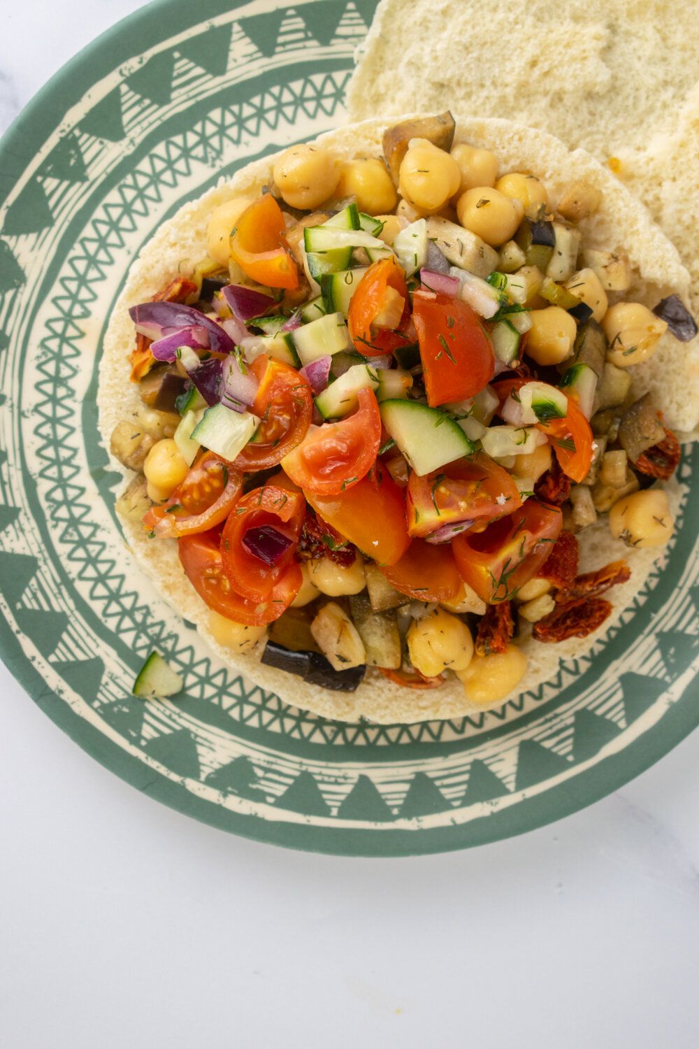 Chickpea tostadas with chickpeas, cucumbers, tomatoes, and red onions on a green plate.