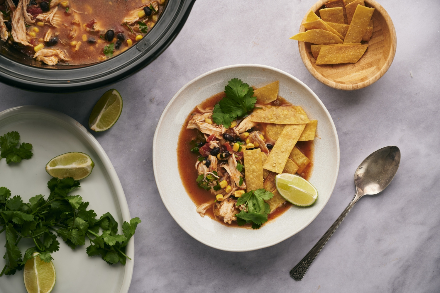 Slow Cooker Chicken Tortilla Soup Slow cooker chicken tortilla soup with shredded chicken, beans, corn, cilantro, crispy tortilla strips, and lime wedges.