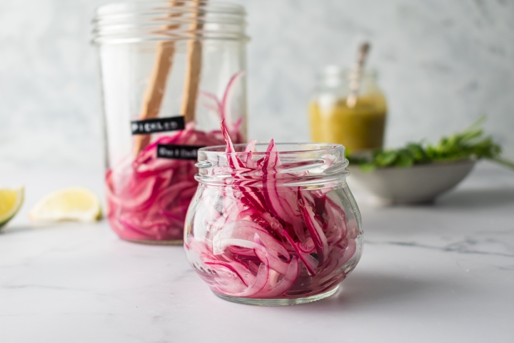 Pickled Red Onions Pickled red onions in a glass jar with lime juice, vinegar, and peppercorns.