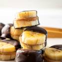 Frozen Banana Bites Stacked banana slices filled with peanut butter, dipped in dark chocolate, arranged artfully on a light background.