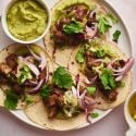 Pork Tacos Pork tacos with crispy pork, red onions, cilantro, and avocado on a plate.