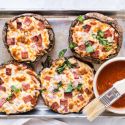 Portobello Mushroom Pizzas Portobello mushroom pizzas on a baking sheet with marinara sauce, melted cheese, basil, ham, and onions.
