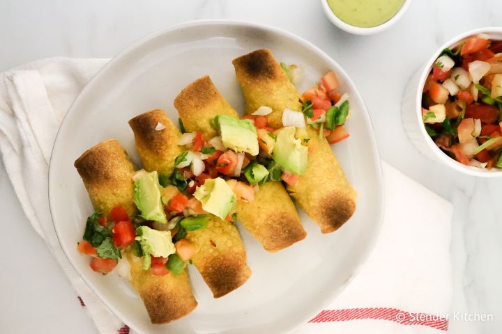 Baked Chicken and Bean Taquitos Chicken Taquitos on a plate with pico de gallo and avocado.