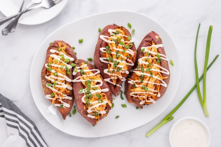 Buffalo Chicken Stuffed Sweet Potatoes Buffalo chicken stuffed sweet potatoes on a plate with ranch dressing and green onions.
