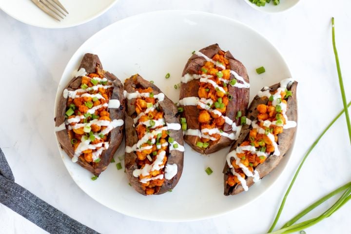 Buffalo Chickpea Stuffed Sweet Potatoes Buffalo chickpea stuffed sweet potatoes on a plate drizzled with ranch dressing and green onions.