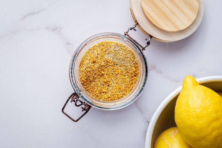 How To Make Lemon Pepper Seasoning Homemade lemon pepper seasoning with dried lemon zest, black pepper, kosher salt, garlic powder, and onion powder in a glass jar.