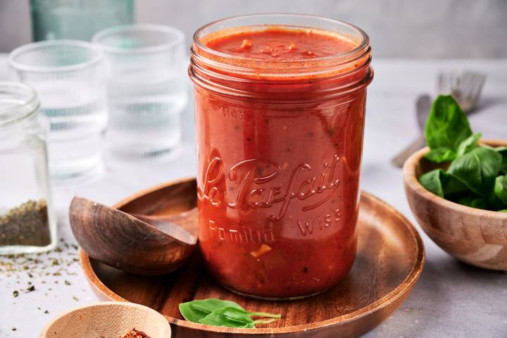 Easy Homemade Marinara Sauce Homemade marinara sauce in a glass jar with flecks of garlic and fresh basil.