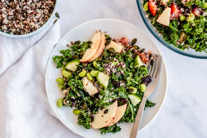 Honey Lime Kale and Quinoa Salad Honey lime kale and quinoa salad with sliced apples, dried cranberries, and pumpkin seeds in a bowl with cooked quinoa on the side.