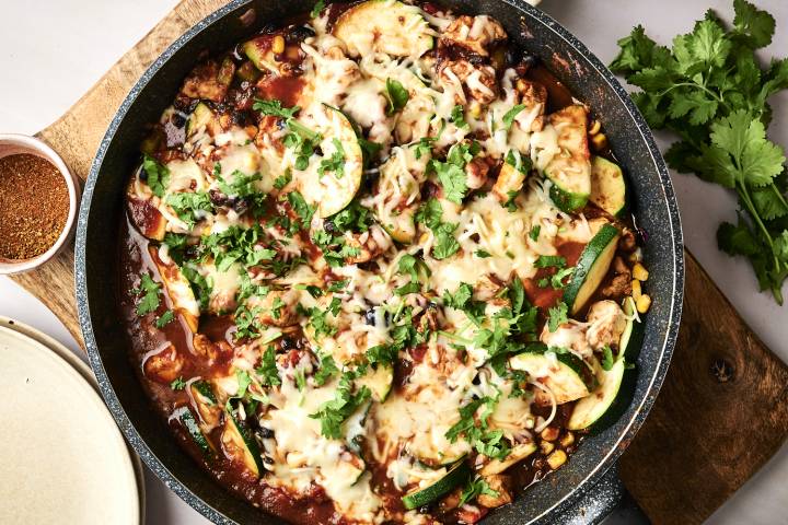 One Pot Mexican Chicken and Zucchini A skillet of cheesy chicken, black beans, and zucchini is served on plates, garnished with fresh cilantro and spices.