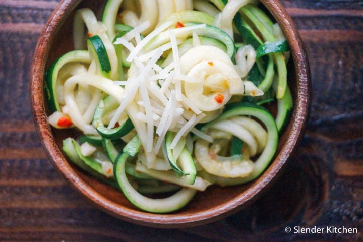Parmesan Zucchini Noodles Parmesan zucchini noodles with shredded Parmesan cheese, red pepper flakes, and black pepper in a wooden bowl.