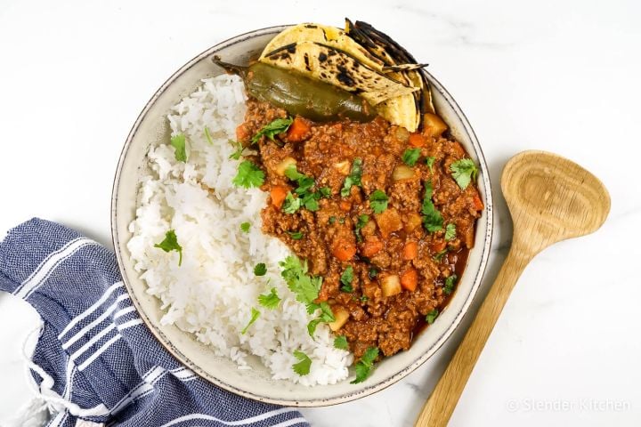 Picadillo Picadillo with potatoes, carrots, and chipotle tomato sauce in a bowl with rice, tortillas, and cilantro.