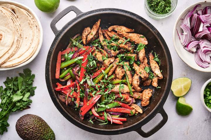 Pork Fajitas Pork fajitas with thin strips of pork, bell peppers, onion, cilantro, and limes in a cast iron skillet.