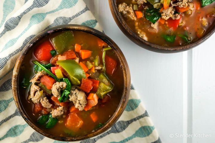 Sausage, Pepper, and Spinach Soup Sausage soup with peppers and spinach in a wooden bowl with carrots, celery, and tomato broth.
