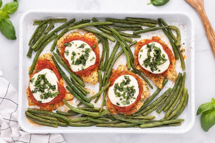 Sheet Pan Healthy Chicken Parm Healthy Chicken Parmesan with breaded chicken covered in sauce and cheese on a sheet pan with roasted green beans.