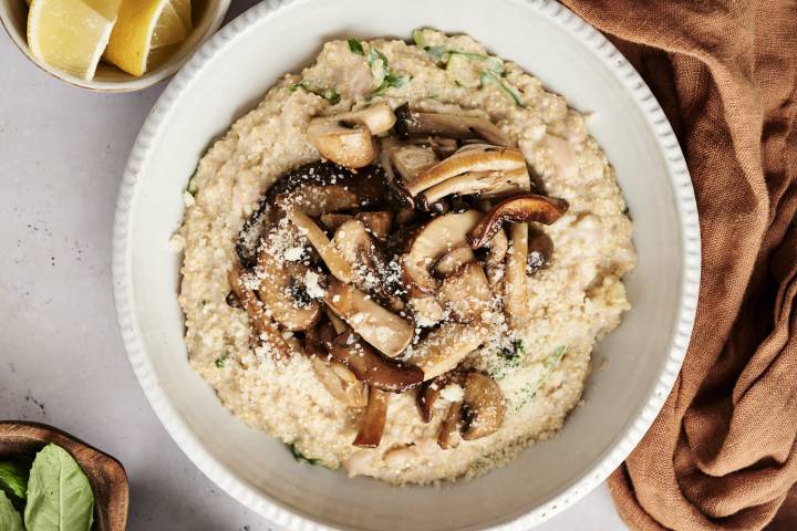 Slow Cooker Garlic Mushroom Quinoa Creamy quinoa topped with sautéed mushrooms and Parmesan cheese, served in a white bowl with lemon wedges on the side.