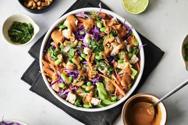 Sweet Chili Chicken Salad A vibrant salad with purple cabbage, carrots, edamame, chicken, and cilantro, drizzled with peanut sauce and topped with cashews.