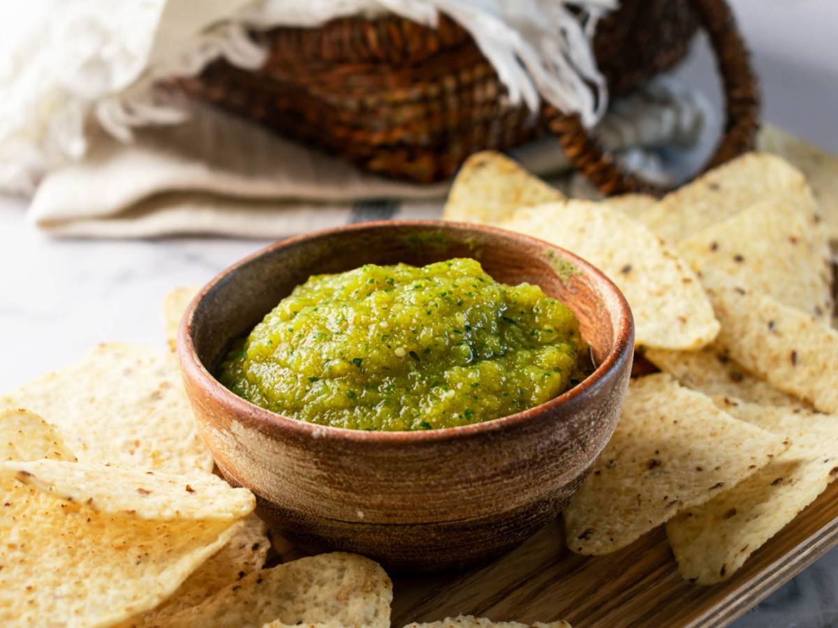 Sauces and Condiments Delicious Mexican salsa verde served on a wooden bowl accompanied by crispy tortilla chips.