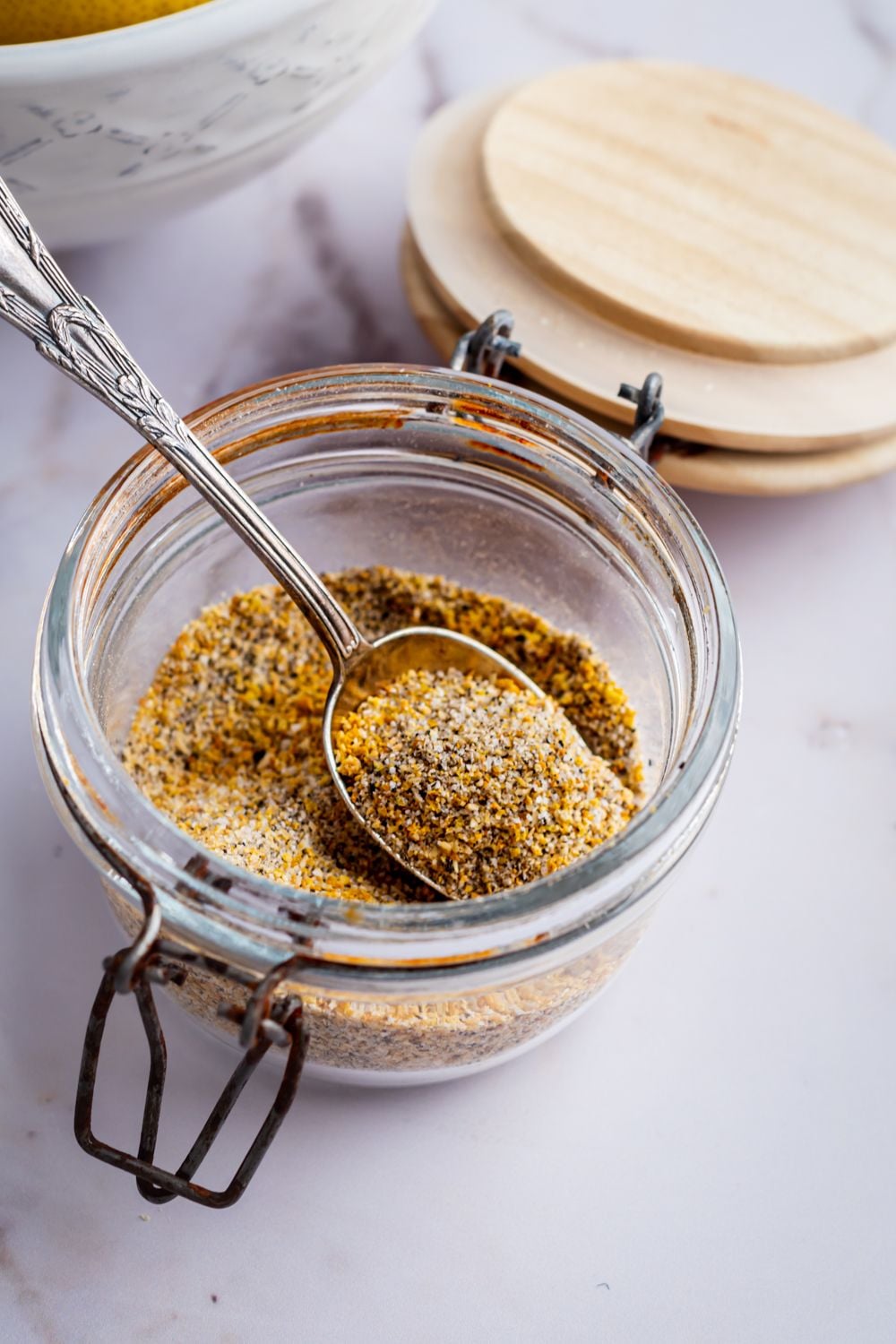 Jar of lemon pepper seasoning with a metal spoon.