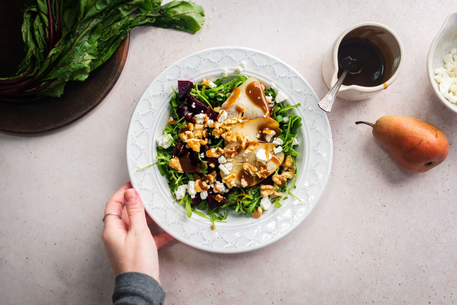 Beet, goat cheese,and arugula salad served with sliced pears and walnuts in a bowl being held by one hand.