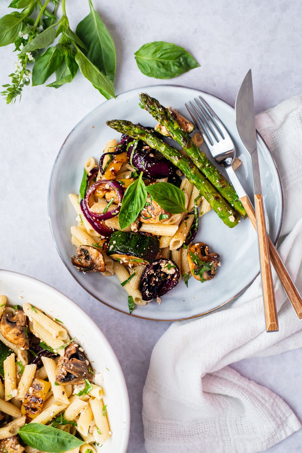 Grilled vegetables and penne paste salad served on two plates with asparagus, onions, peppers, mushrooms, and zucchini.