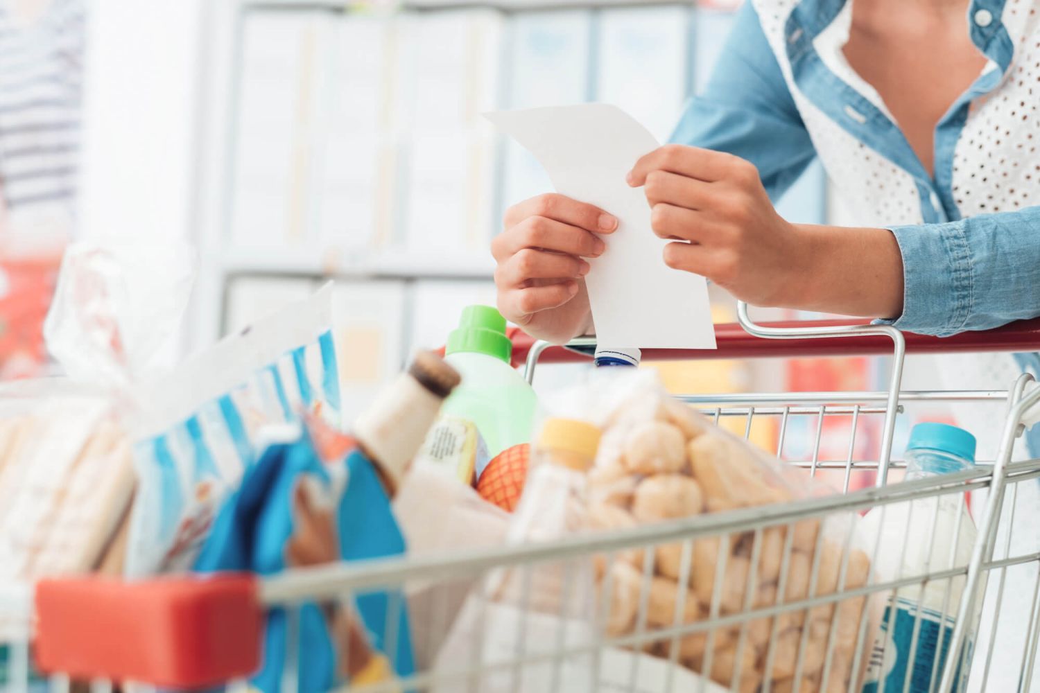Grocery cart with woman with a list in her hand.