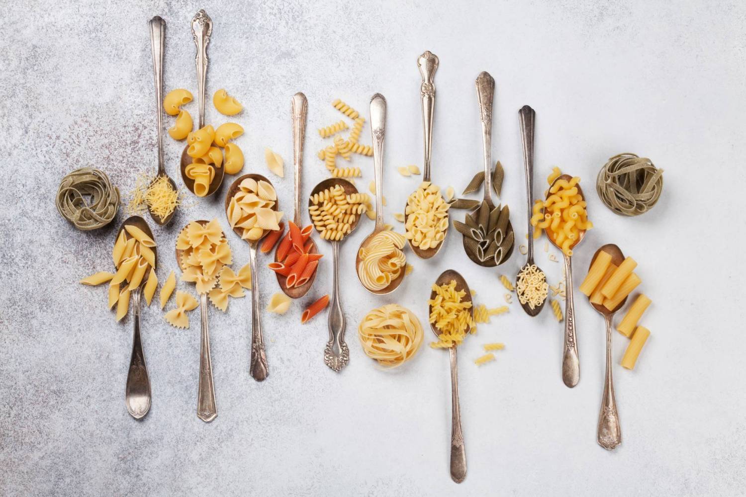 Different types of pasta including whole wheat pasta, chickpea pasta, lentil pasta, and different pasta shapes on spoons.