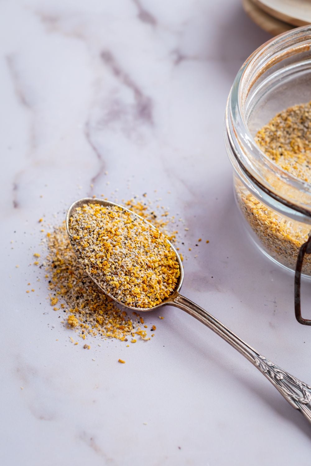 Lemon pepper spice blend in glass jar with dried lemon zest, black pepper, kosher salt, and garlic powder.
