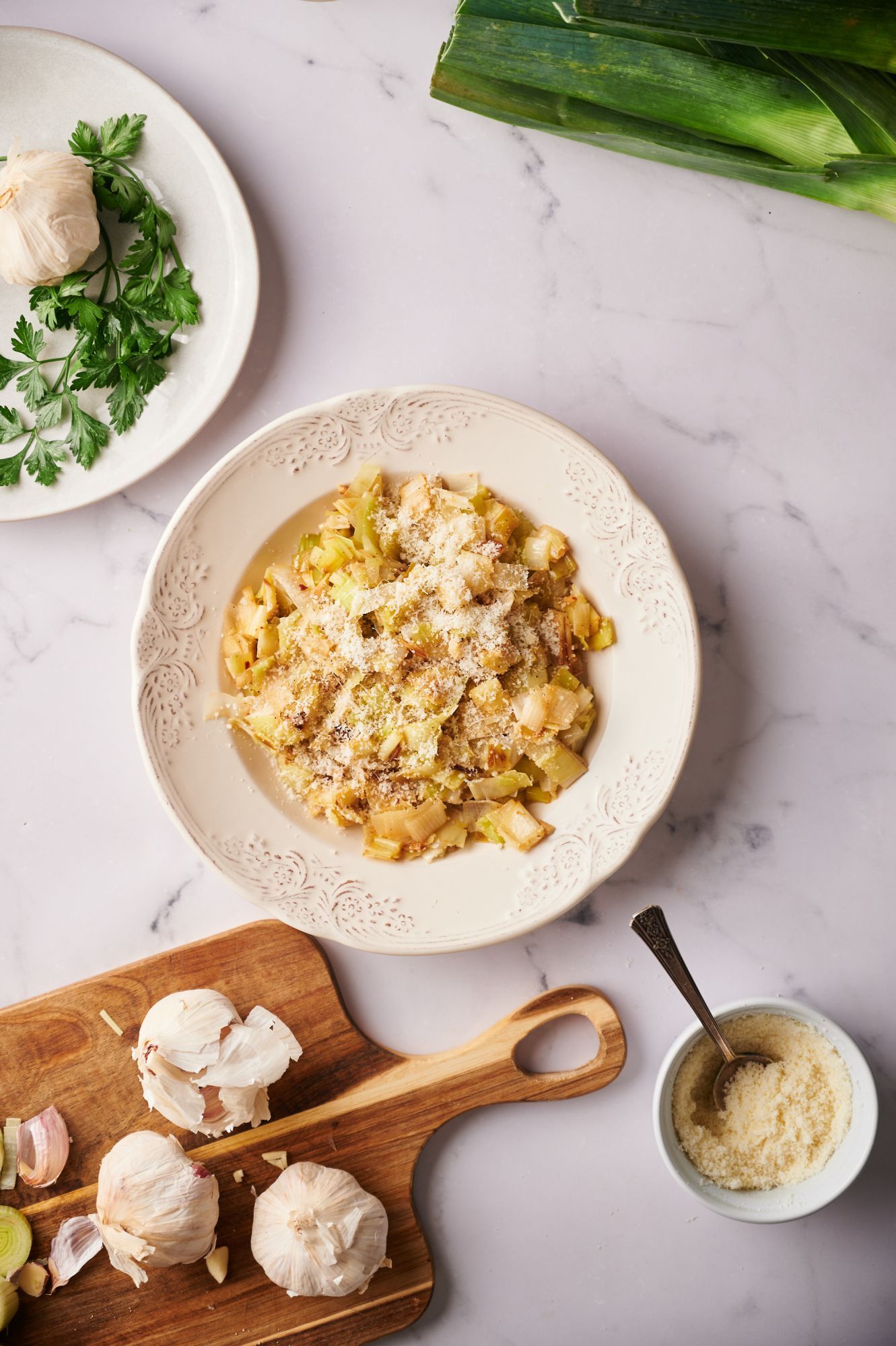 Leeks sautéed in butter and served with Parmesan cheese in a bowl with garlic and herbs on the side.