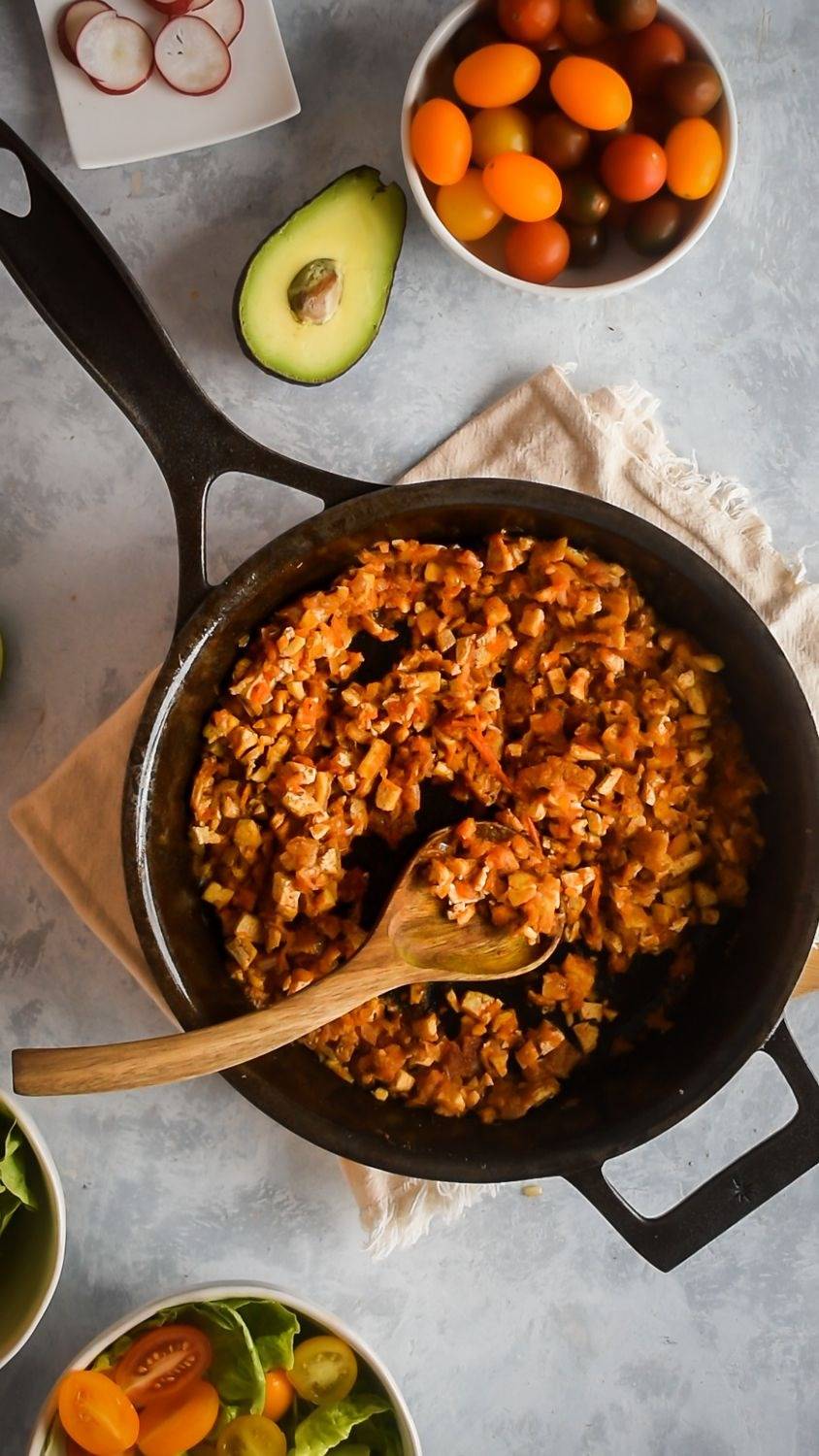 Tofu Sofritas in chipotle tomato sauce in a skillet with a wooden spoon.