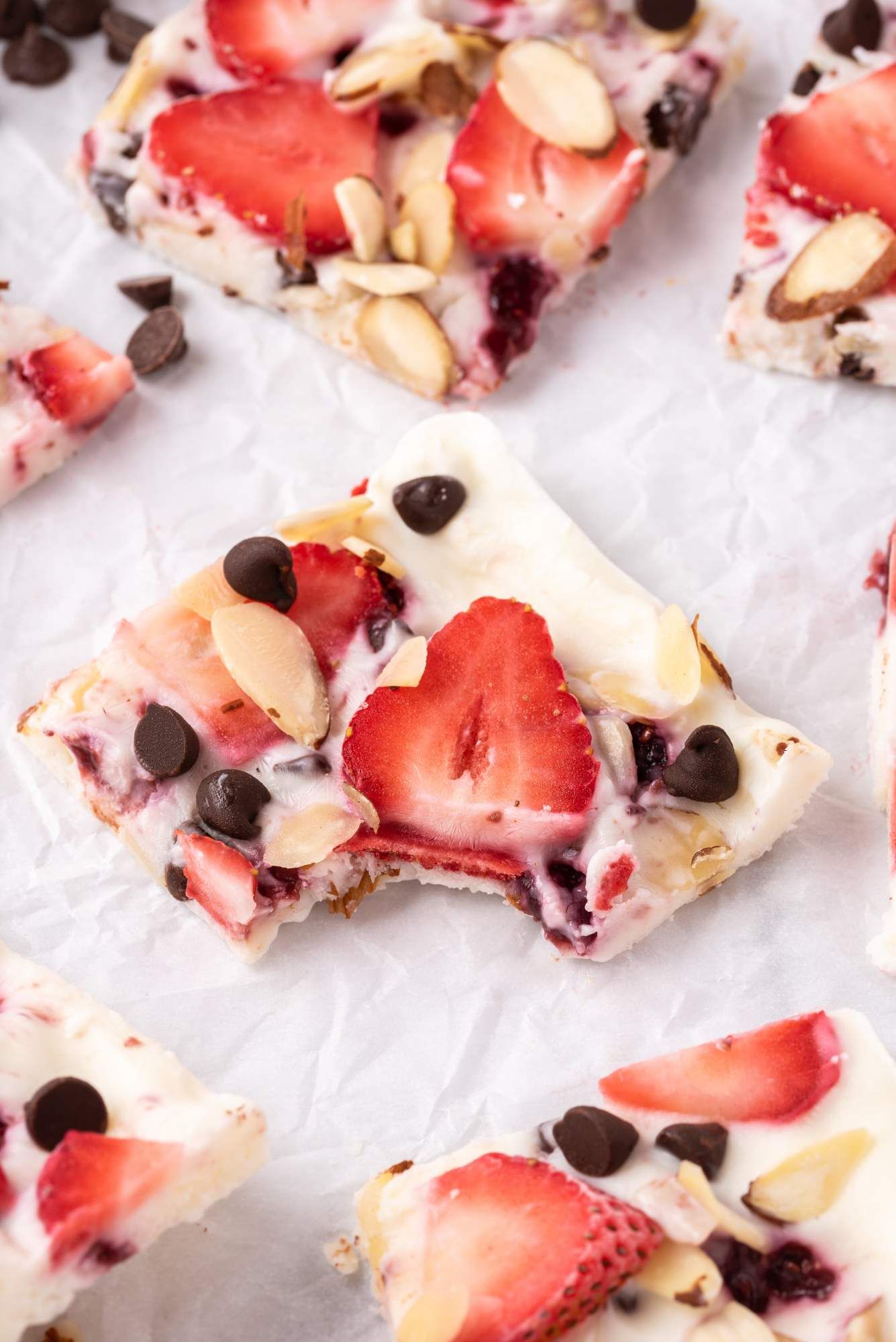 Yogurt bark with Greek yogurt, strawberries, almonds, chocolate chips on a piece of parchment paper.