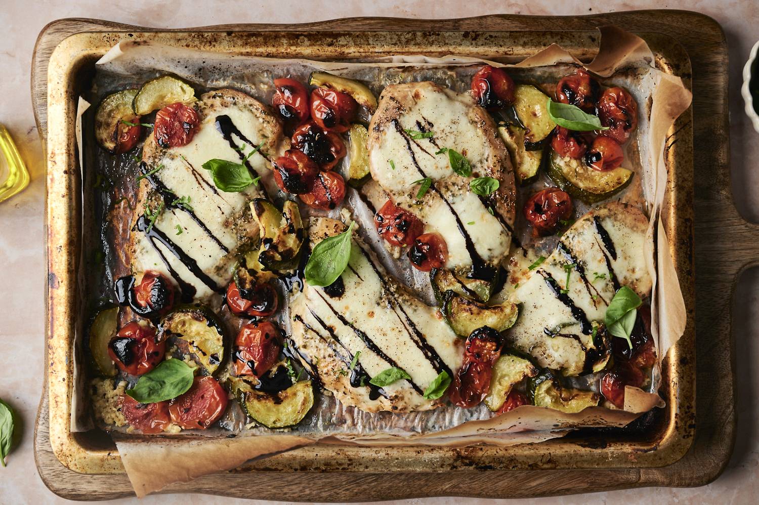 Sheet pan Caprese chicken, with roasted zucchini, cherry tomatoes, fresh basil, and a balsamic glaze drizzled over the melted mozzarella on the chicken breasts.