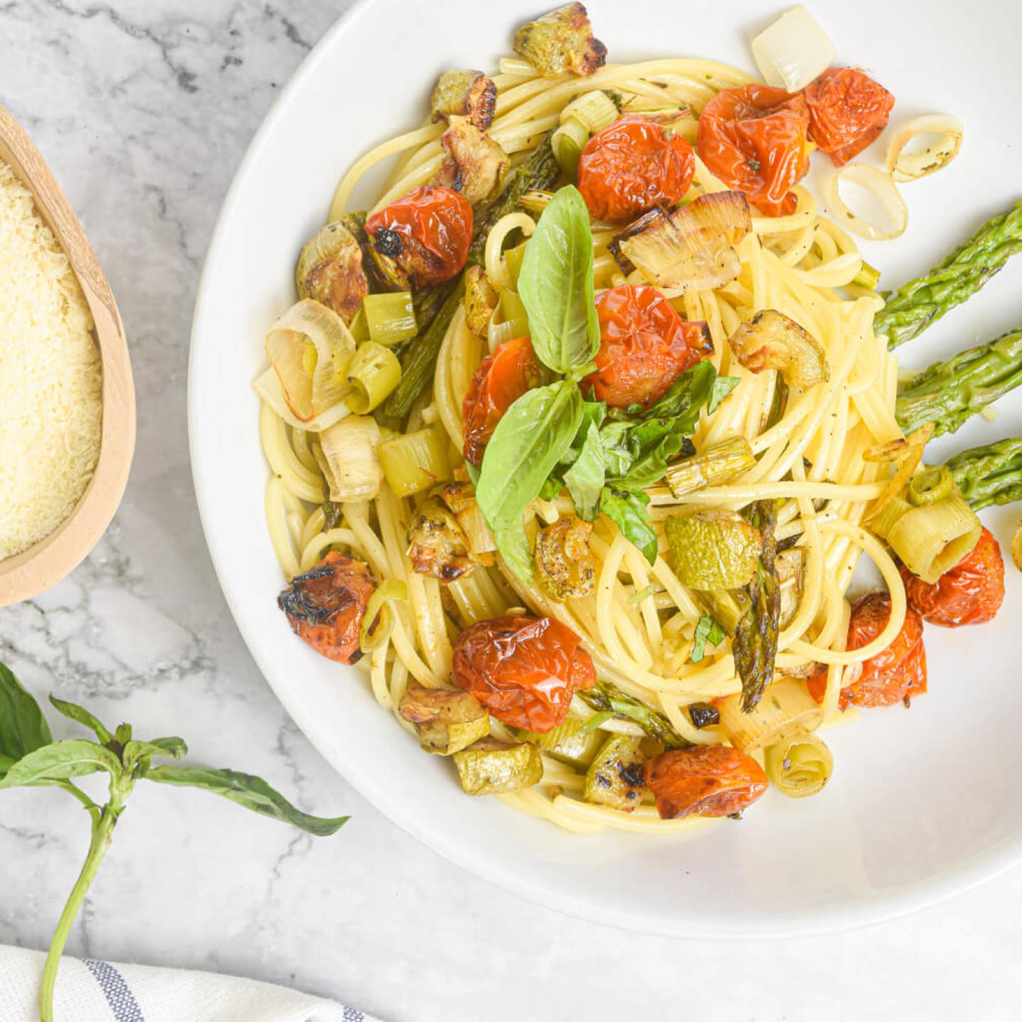 Roasted vegetable pasta with tomatoes, asparagus, onions, and leeks with Parmesan and basil on the side.