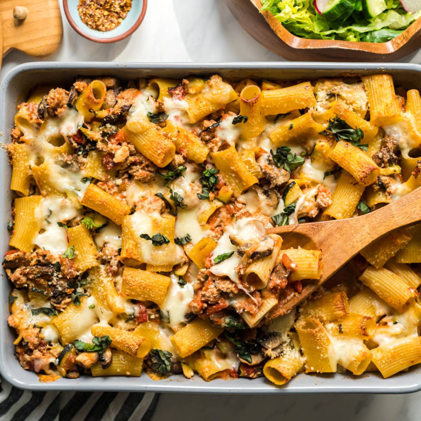 Baked ziti with ground beef, tomatoes, zucchini, and melted cheese in a baking dish.