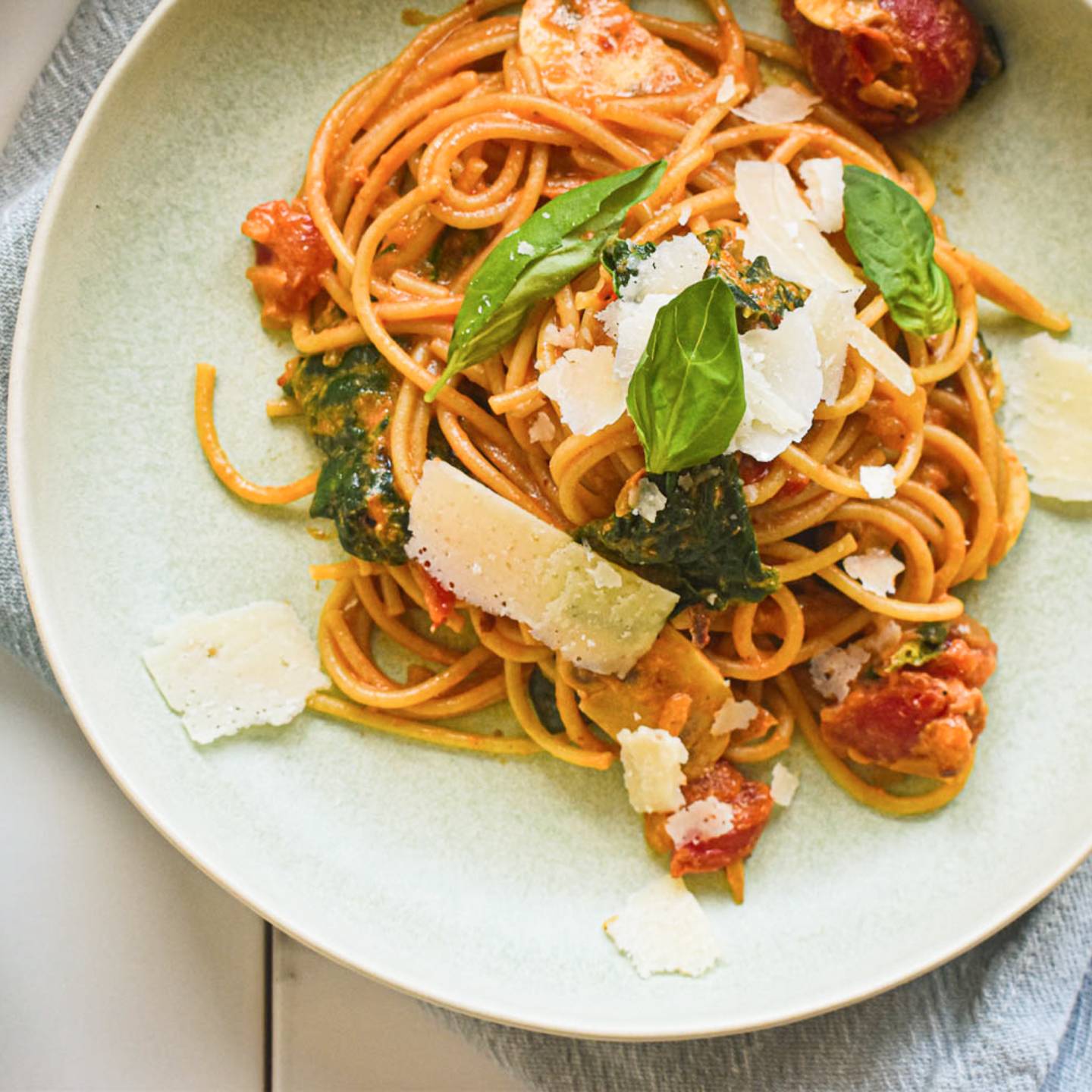 Creamy tomato mushroom and spinach pasta on a plate with whole grain pasta, creamy sauce, spinach, mushrooms, and parmesan cheese.