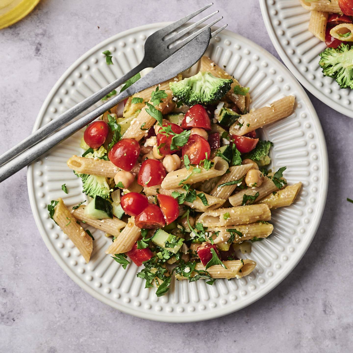 A vibrant plate of pasta mixed with cherry tomatoes, broccoli, and herbs, accompanied by a glass of olive oil and fresh basil leaves.