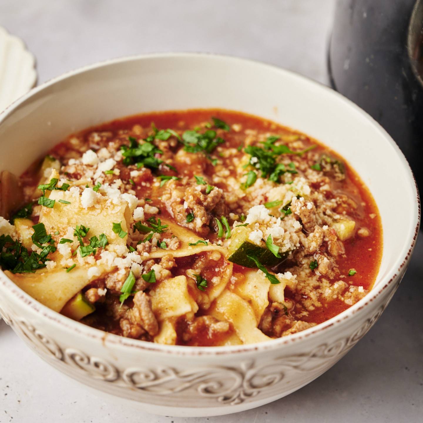 A bowl of lasagna soup with a rich tomato broth, ground meat, zucchini, and lasagna noodles, topped with parmesan cheese and fresh parsley.