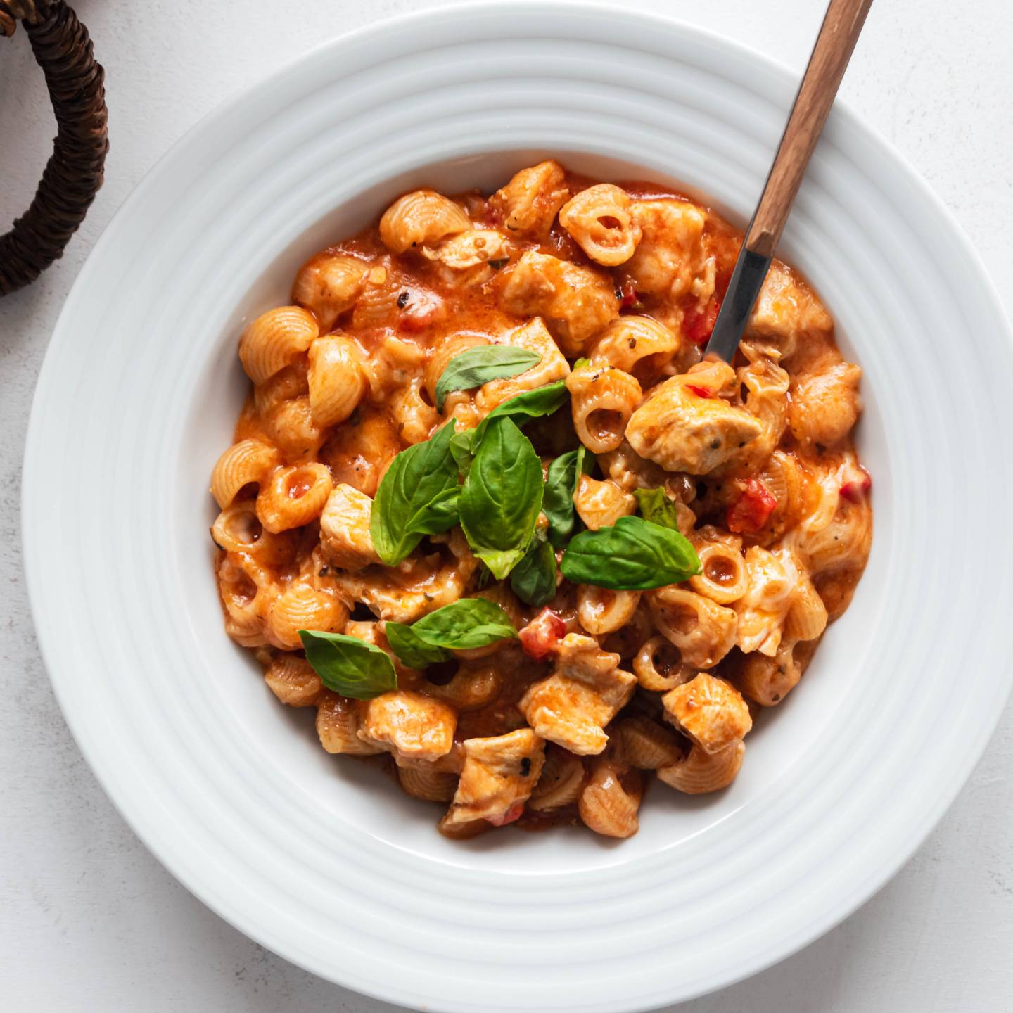One pot chicken pasta with marinara sauce, chicken breast, melted cheese, and fresh basil in a bowl.