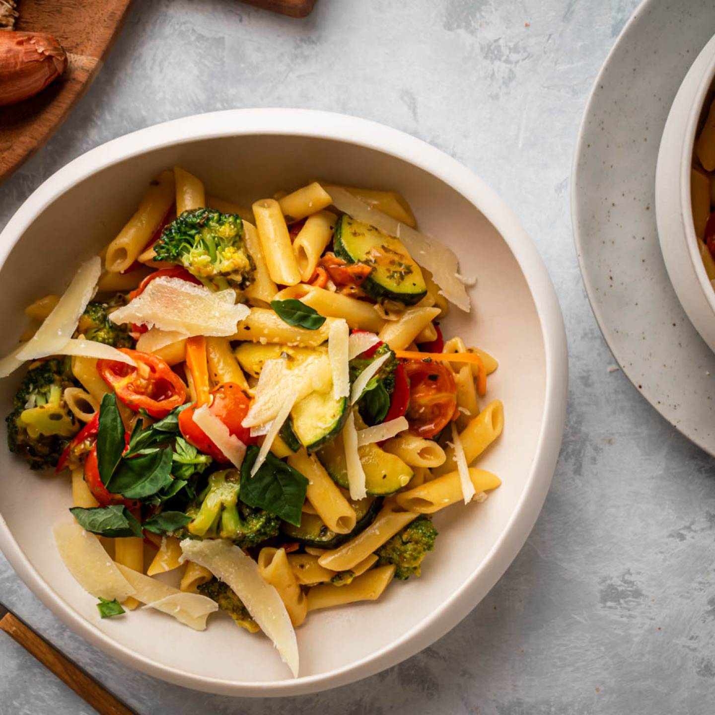 Pasta primavera in a bowl with zucchini, broccoli, carrots, cherry tomatoes, Parmesan cheese, and fresh basil.