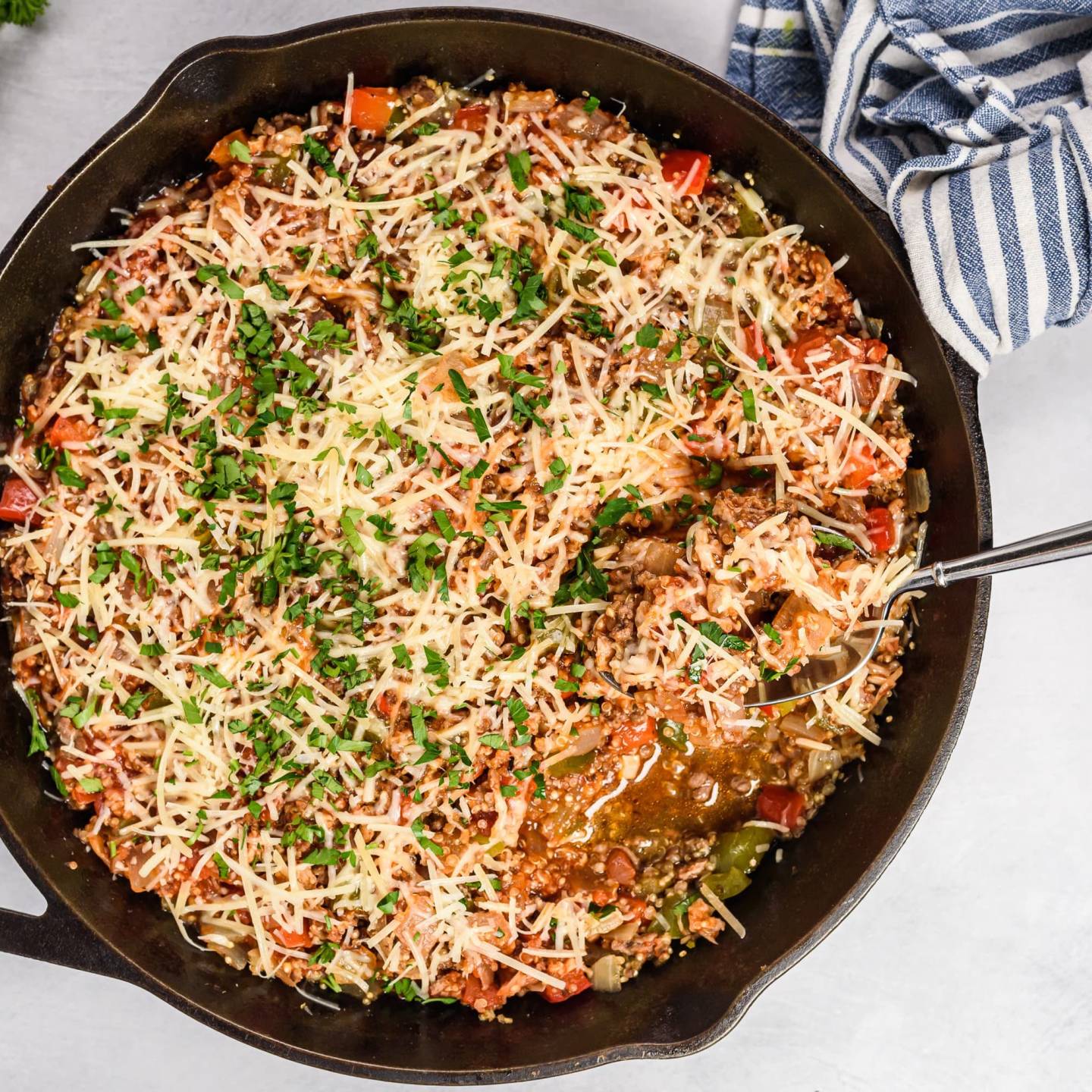 Unstuffed pepper skillet with ground beef, turkey sausage, quinoa, and bel peppers in a cast iron skillet topped with Parmesan cheese.