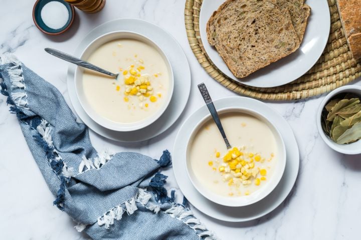 Corn chowder made with fresh corn, cauliflower, onions, milk, and spices in two bowls with bread on the side.