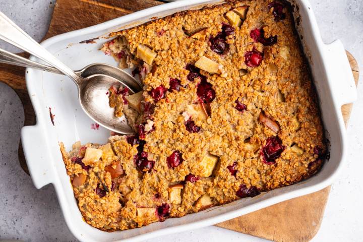 Golden-baked oatmeal casserole with cranberry and apple chunks in a white dish. 
