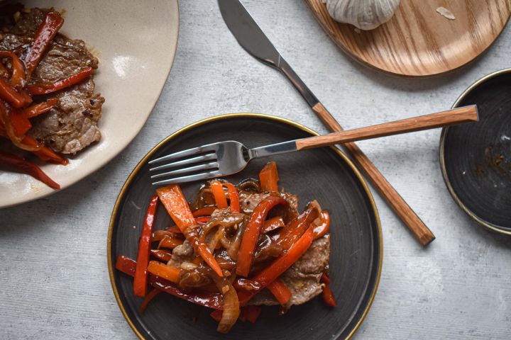 Pepper steak with thinly sliced sirloin steak, bell peppers, onions, and a peppery stir fry sauce on a plate with rice. 