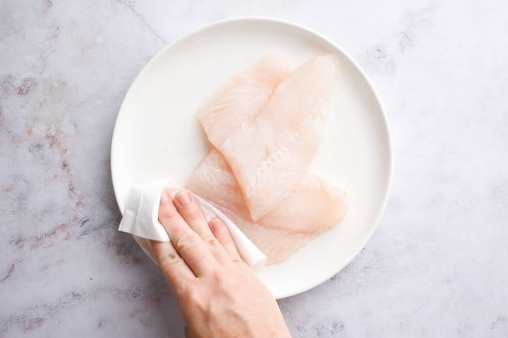 Fish fillets being patted with a paper towel.