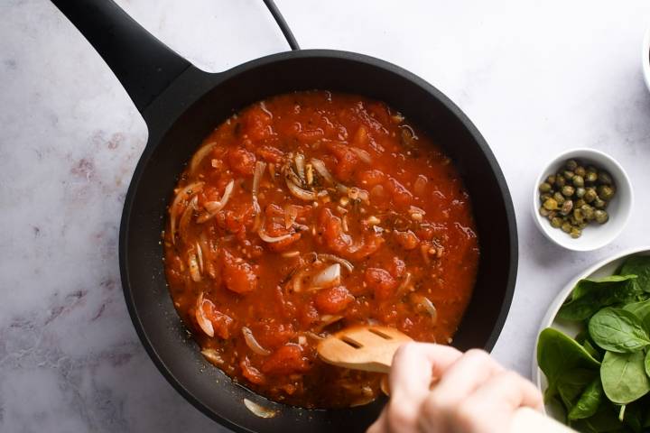 Tomatoes simmering in a skillet with spices and onions.
