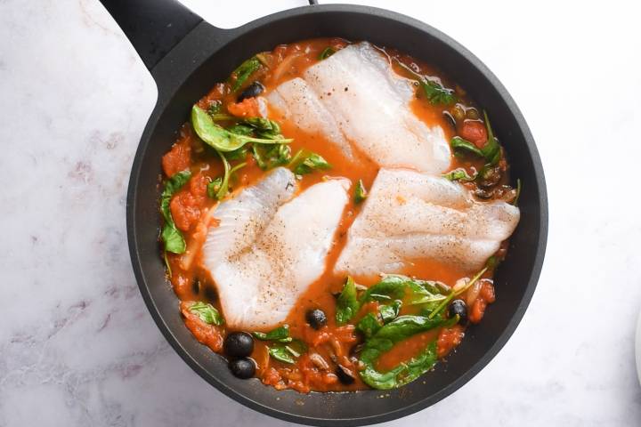 Cod fillets in a skillet with a Mediterranean tomato sauce.