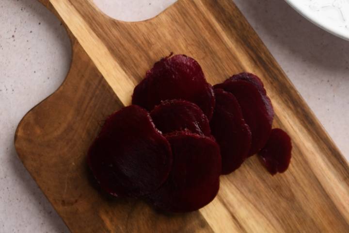 Sliced roasted beets on a wooden cutting board.