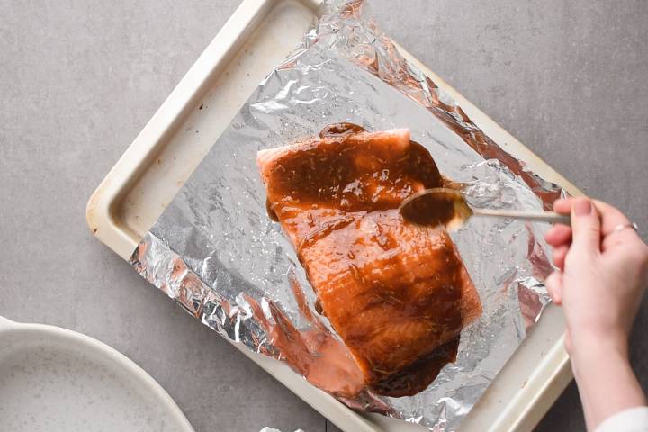 Salmon being brushed with brown sugar glaze on a baking sheet.
