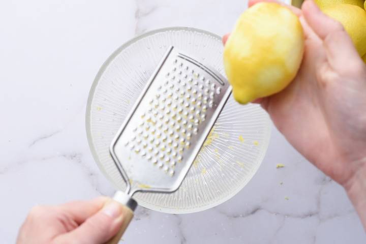 Lemon zest being grated into a glass bowl.