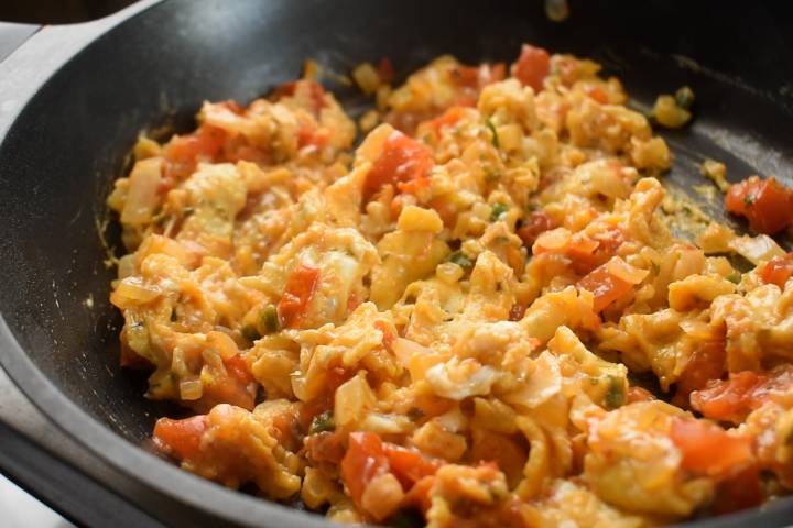 Scrambled eggs with tomatoes, onions, and jalapenos in a skillet.