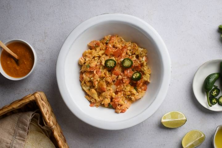 Huevos a la mexicana in a bowl wiht sliced jalapenos and ranchero sauce on the side.